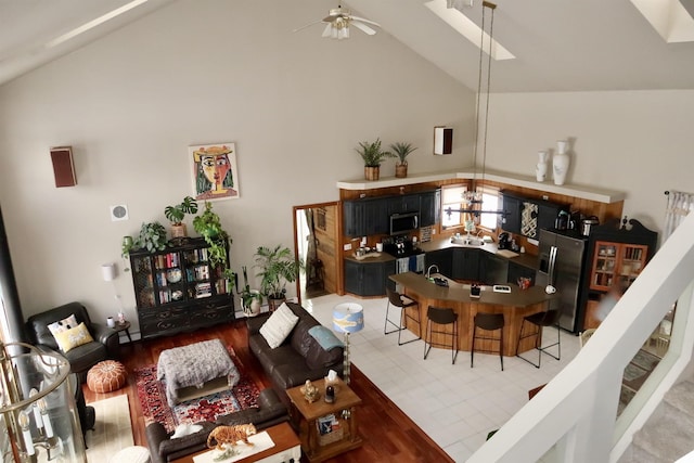 living area with high vaulted ceiling, a skylight, and a ceiling fan