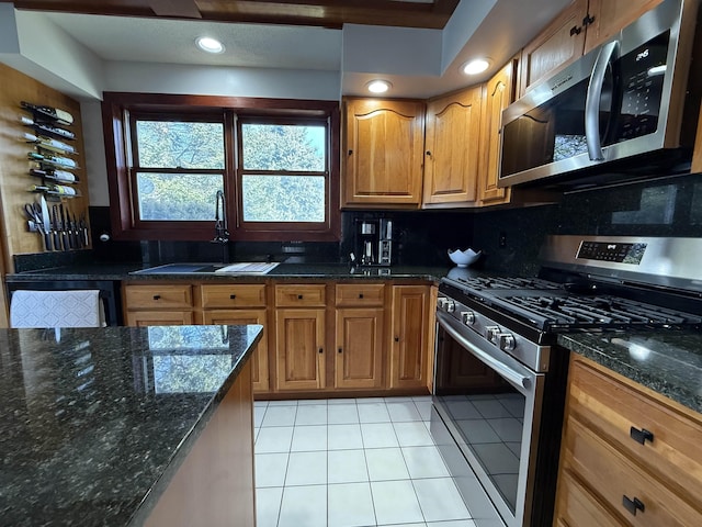 kitchen with a sink, dark stone countertops, tasteful backsplash, appliances with stainless steel finishes, and light tile patterned floors