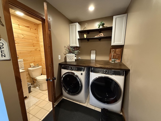 clothes washing area with wooden walls, light tile patterned flooring, cabinet space, and independent washer and dryer