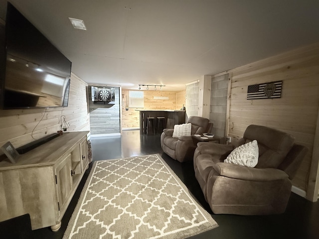 living room featuring concrete flooring, wood walls, and track lighting