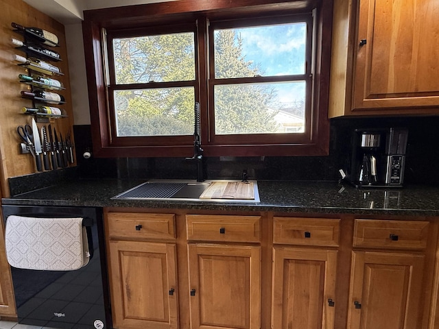 kitchen featuring dark stone countertops, brown cabinets, black dishwasher, and a sink