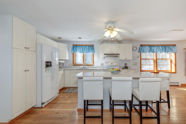 kitchen featuring white appliances, light wood-style flooring, light countertops, a baseboard heating unit, and a kitchen breakfast bar