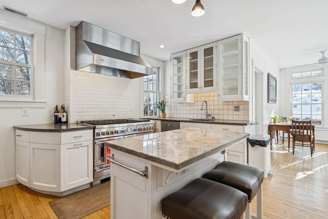 kitchen featuring dark stone counters, a sink, stainless steel appliances, wall chimney range hood, and light wood-type flooring