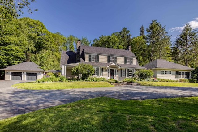 view of front of house featuring an outdoor structure, a garage, a front yard, and a chimney