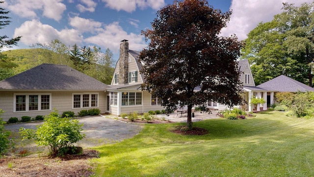 view of front facade with a patio area, a chimney, a front yard, and roof with shingles