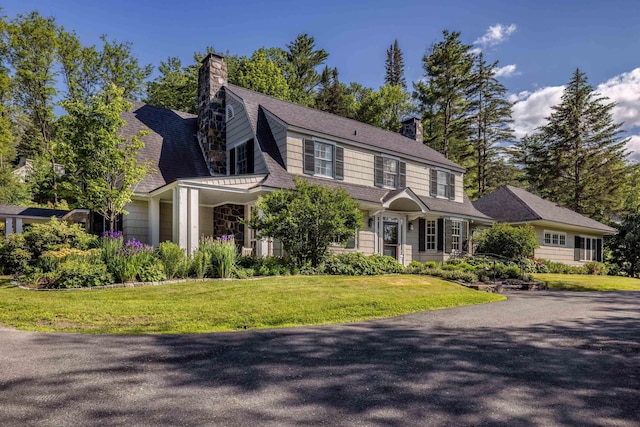 dutch colonial with a front lawn, roof with shingles, and a chimney