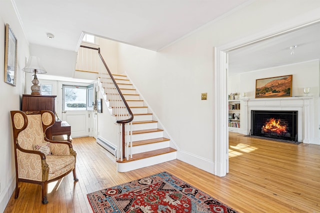 stairs with hardwood / wood-style floors, baseboards, a fireplace with flush hearth, ornamental molding, and baseboard heating