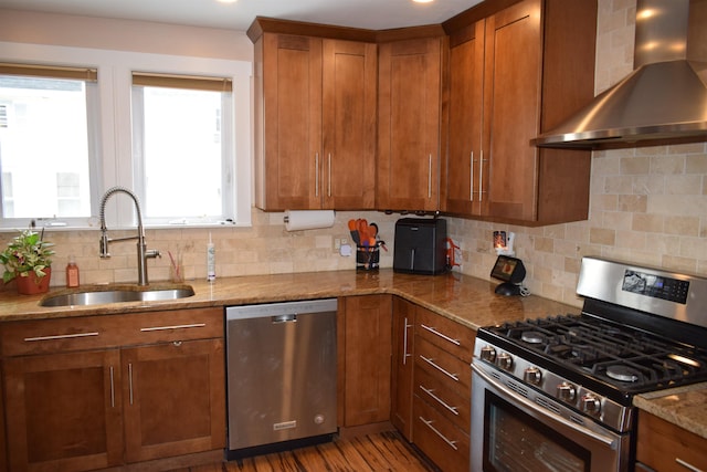 kitchen featuring a sink, wall chimney range hood, brown cabinetry, and stainless steel appliances