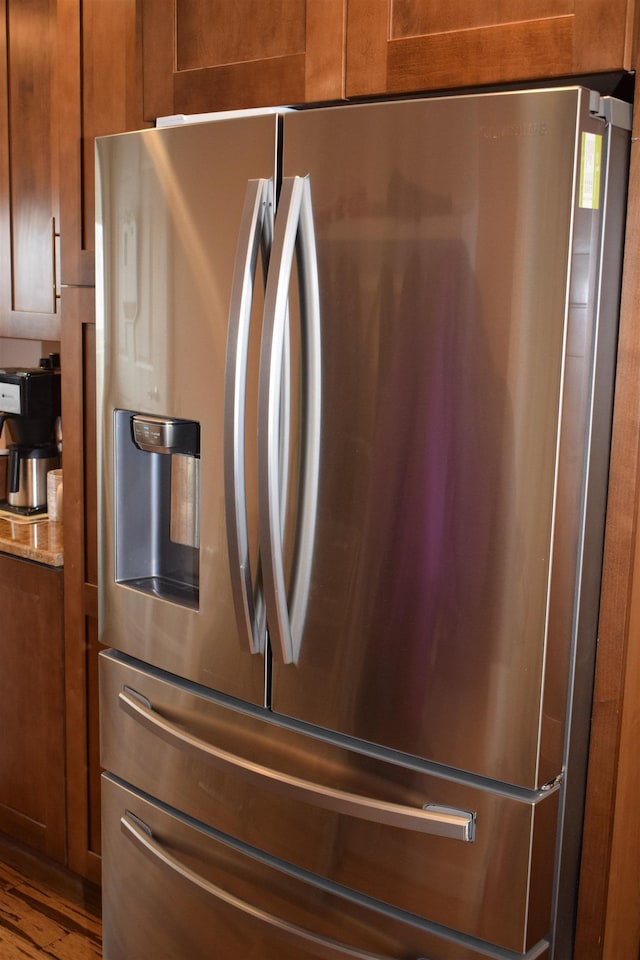 kitchen featuring brown cabinetry, stainless steel fridge, and light stone counters