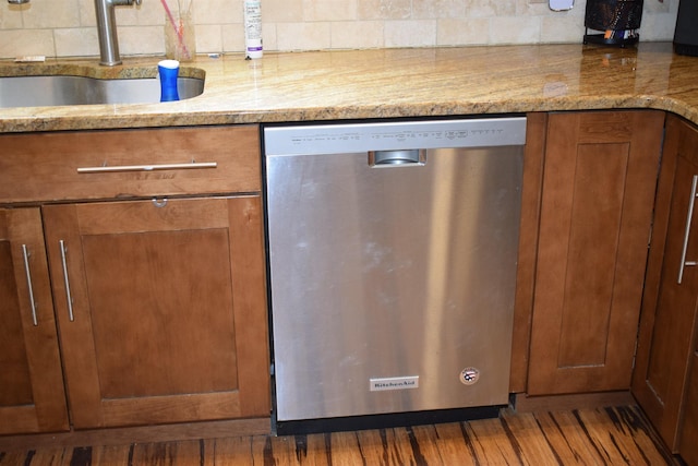 kitchen featuring wood finished floors, brown cabinetry, a sink, dishwasher, and tasteful backsplash