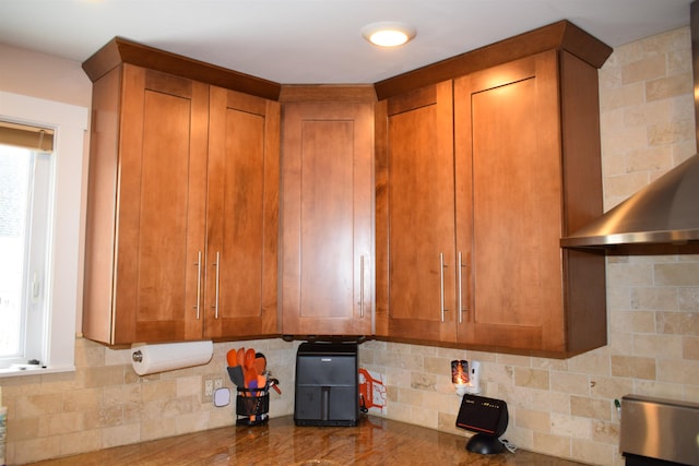 kitchen featuring decorative backsplash, wall chimney exhaust hood, and brown cabinetry