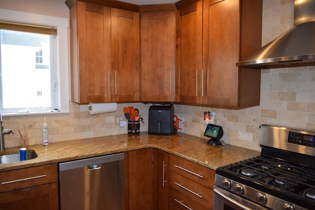 kitchen with brown cabinetry, plenty of natural light, appliances with stainless steel finishes, and wall chimney range hood