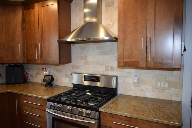 kitchen featuring decorative backsplash, wall chimney range hood, light stone counters, and stainless steel range with gas stovetop