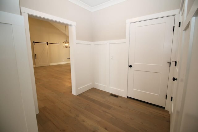 hall with visible vents, a barn door, wainscoting, wood finished floors, and a decorative wall