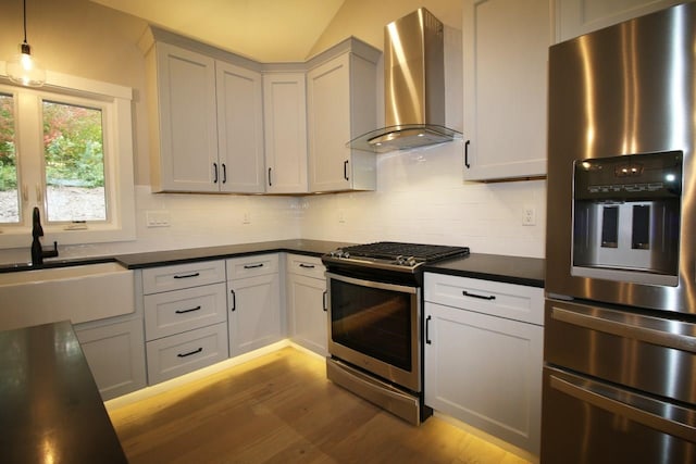 kitchen with a sink, stainless steel appliances, dark countertops, wall chimney exhaust hood, and backsplash