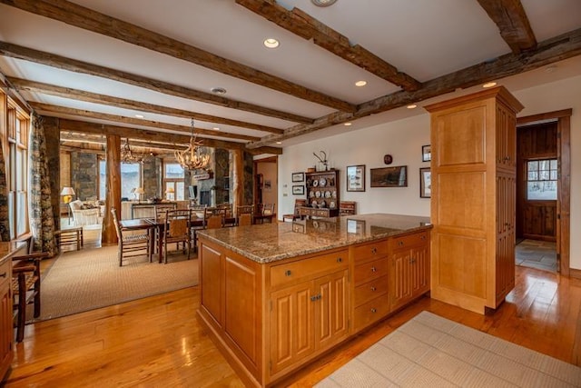 kitchen featuring dark stone countertops, beamed ceiling, light wood-style floors, and a chandelier