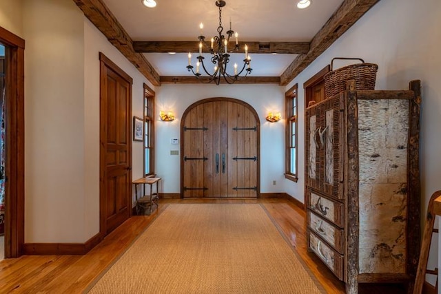 foyer featuring arched walkways, beamed ceiling, baseboards, and wood finished floors