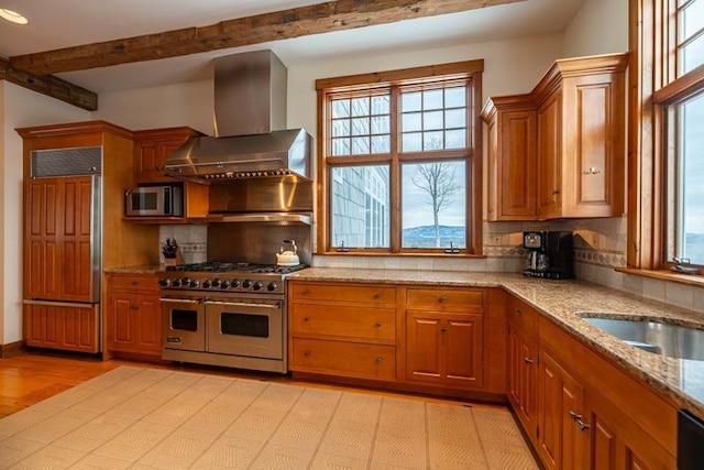 kitchen with backsplash, beam ceiling, premium appliances, light stone counters, and wall chimney exhaust hood