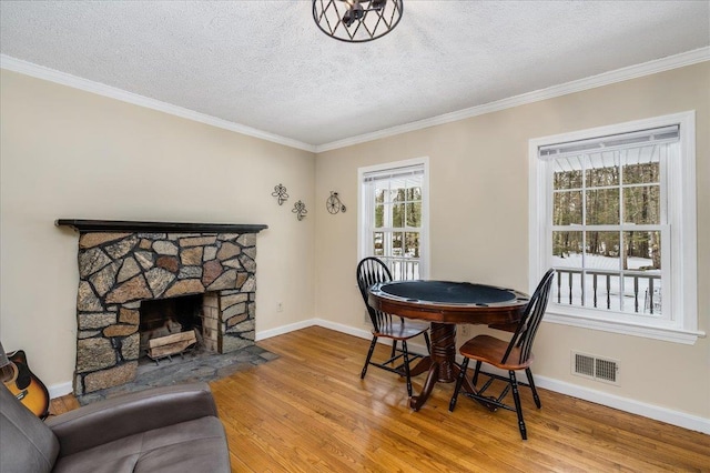 dining space with visible vents, ornamental molding, wood finished floors, a fireplace, and baseboards