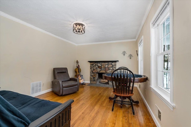 sitting room with a stone fireplace, light wood-style floors, visible vents, and ornamental molding