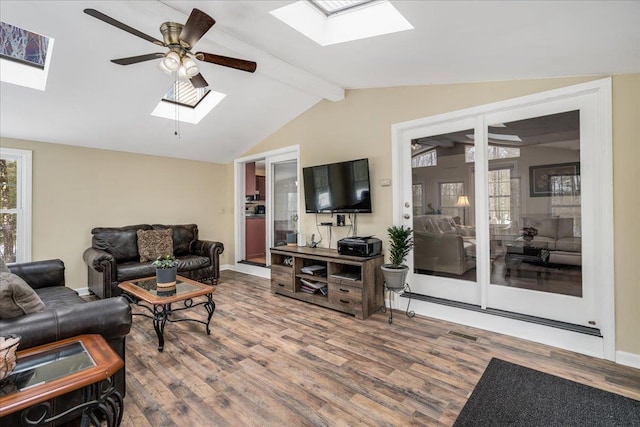 living area featuring ceiling fan, vaulted ceiling with skylight, plenty of natural light, and wood finished floors