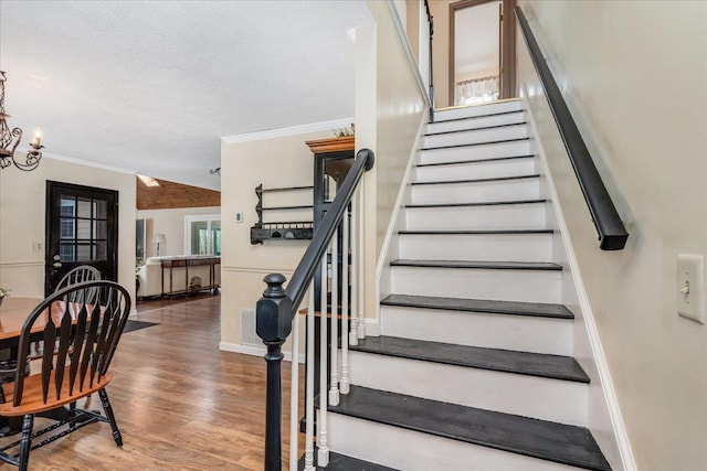 stairs featuring a notable chandelier, ornamental molding, a textured ceiling, wood finished floors, and baseboards