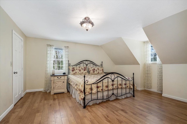 bedroom with light wood-type flooring, baseboards, and vaulted ceiling