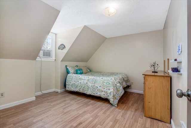 bedroom featuring light wood finished floors, baseboards, vaulted ceiling, cooling unit, and a textured ceiling