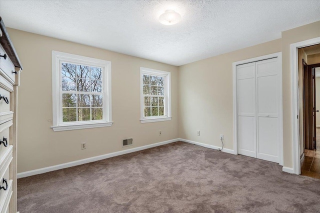 unfurnished bedroom featuring visible vents, baseboards, carpet, a closet, and a textured ceiling