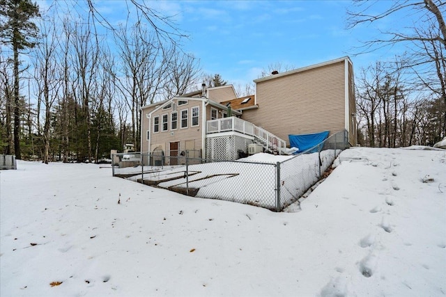 snow covered back of property with a wooden deck, a garage, and fence