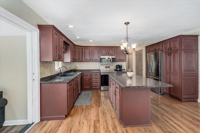 kitchen featuring dark countertops, a center island, light wood-style flooring, stainless steel appliances, and a sink