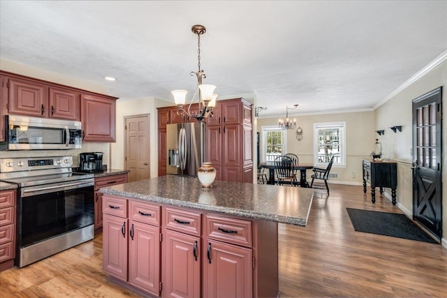 kitchen with a kitchen island, light wood-style flooring, appliances with stainless steel finishes, dark countertops, and a notable chandelier