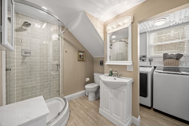 bathroom featuring a shower stall, toilet, wood finished floors, and washing machine and clothes dryer