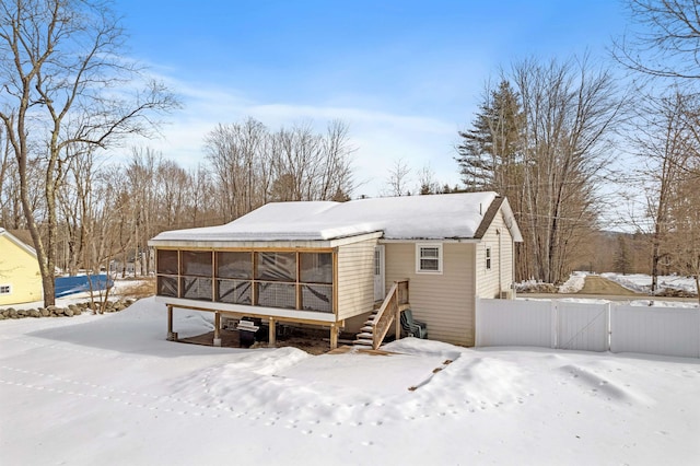 snow covered back of property featuring a gate, fence, a garage, and a sunroom