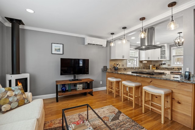 kitchen featuring glass insert cabinets, a wall unit AC, island exhaust hood, a wood stove, and gas cooktop