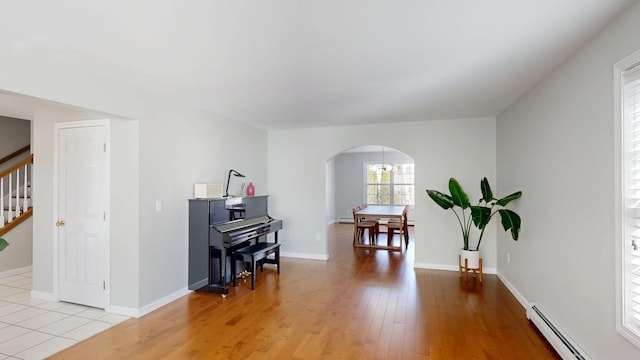 sitting room featuring light wood finished floors, baseboards, stairway, baseboard heating, and arched walkways