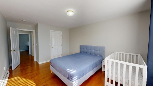 bedroom with a baseboard heating unit, wood finished floors, baseboards, and a baseboard radiator