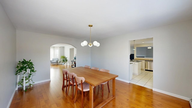 dining room featuring baseboards, arched walkways, and light wood-style flooring