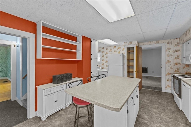 kitchen featuring white appliances, a kitchen island, white cabinets, and wallpapered walls