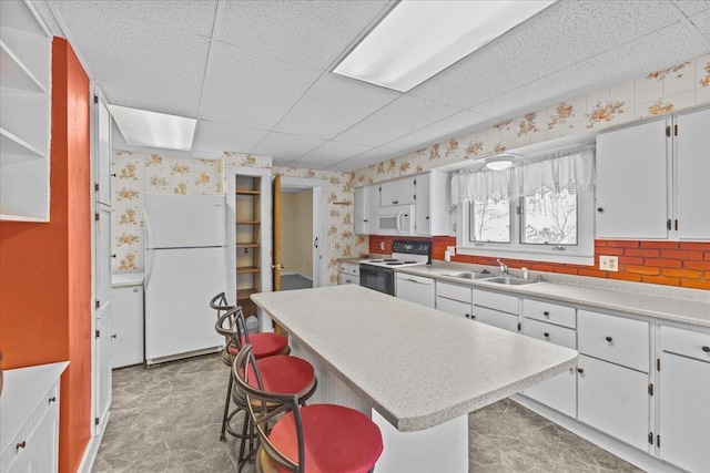 kitchen with wallpapered walls, light countertops, white cabinets, white appliances, and a sink