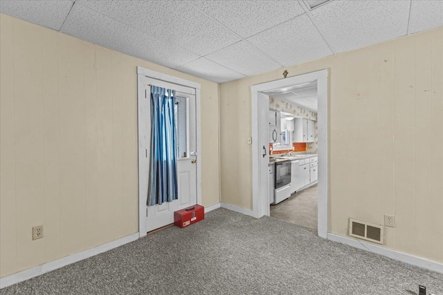 empty room with visible vents, baseboards, wood walls, carpet floors, and a paneled ceiling