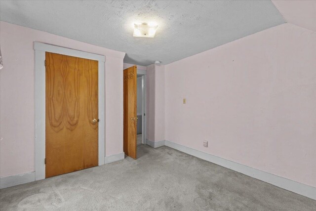 unfurnished bedroom with carpet flooring, a textured ceiling, and vaulted ceiling