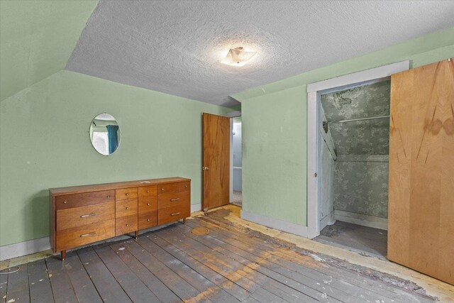 unfurnished bedroom with dark wood finished floors, vaulted ceiling, baseboards, and a textured ceiling