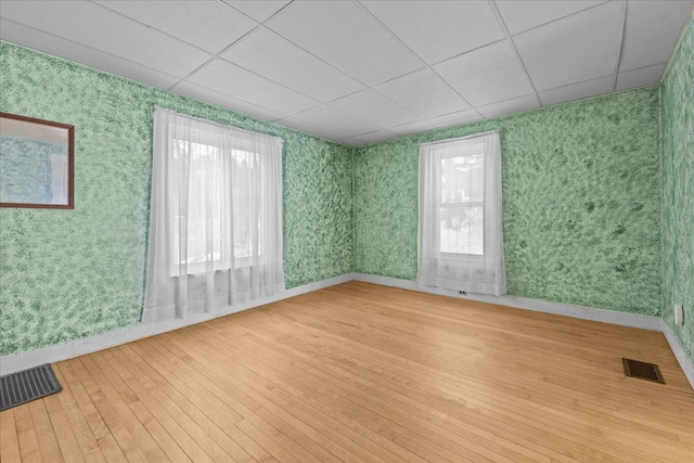 unfurnished room featuring visible vents, a drop ceiling, wallpapered walls, and hardwood / wood-style flooring