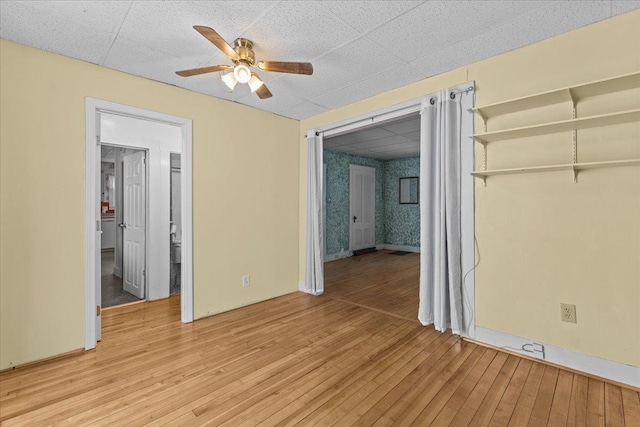 unfurnished room with a drop ceiling, a ceiling fan, and light wood-style floors