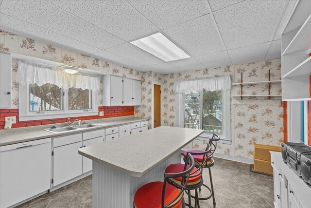 kitchen with wallpapered walls, light countertops, white dishwasher, white cabinetry, and a sink