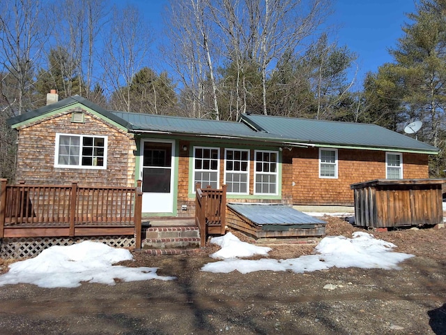 snow covered house with a deck, a hot tub, and metal roof