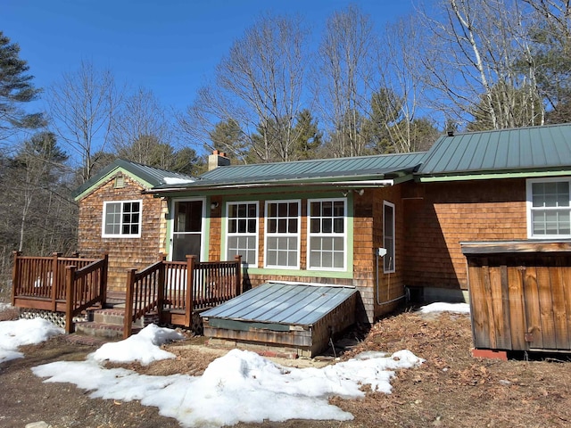 single story home with metal roof, a deck, a chimney, and a standing seam roof