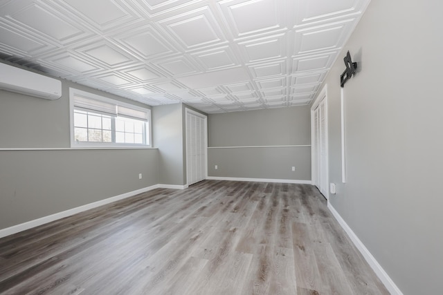 unfurnished room featuring a wall unit AC, light wood-style floors, baseboards, and an ornate ceiling