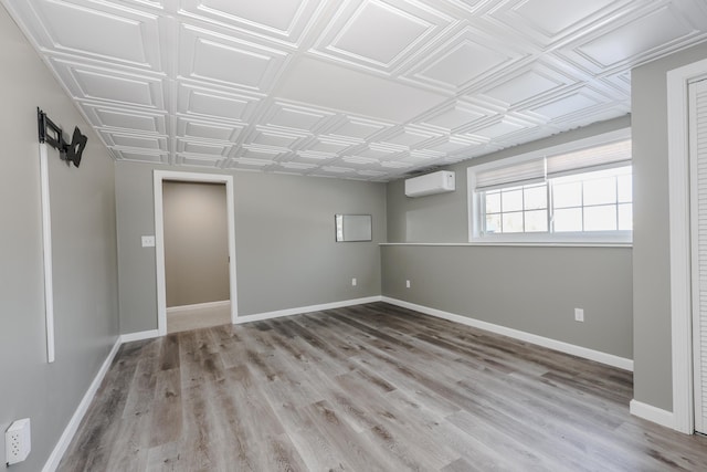 unfurnished room featuring a wall mounted air conditioner, wood finished floors, baseboards, and an ornate ceiling